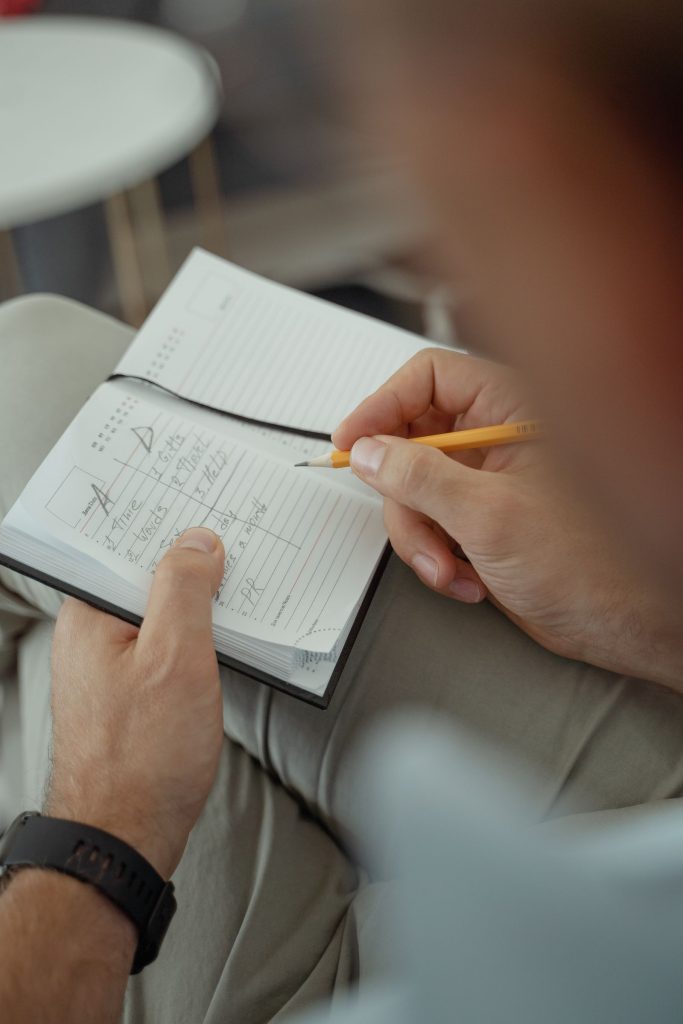 A man writing in a notebook with a pencil.