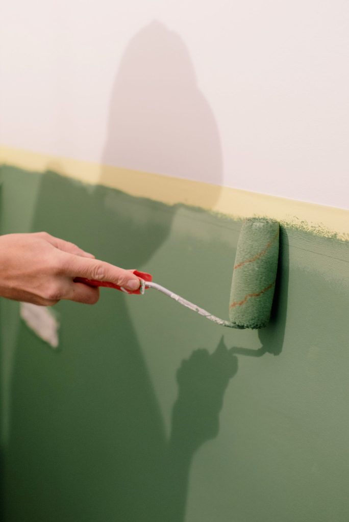 A paint roller putting green paint on a wall.