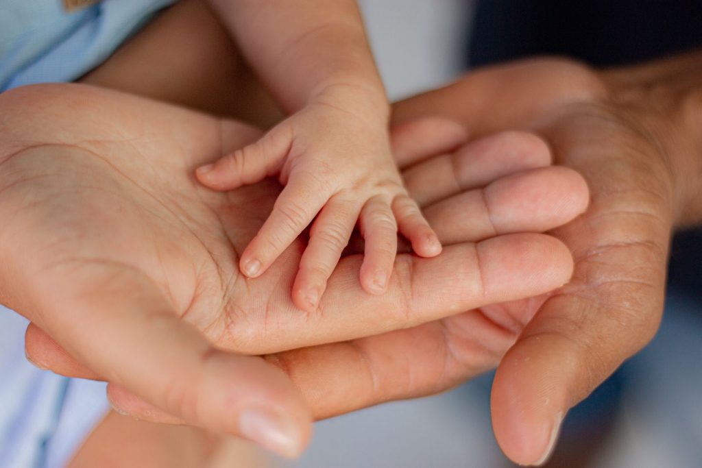 Hands from three generations holding a newborn's tiny hand.
