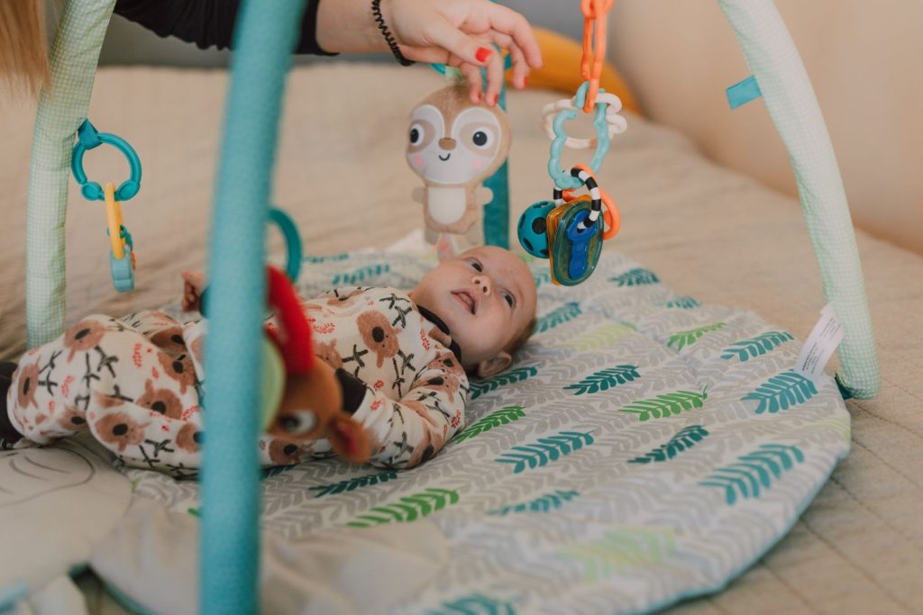 A baby on a play mat reaching for hanging toys.