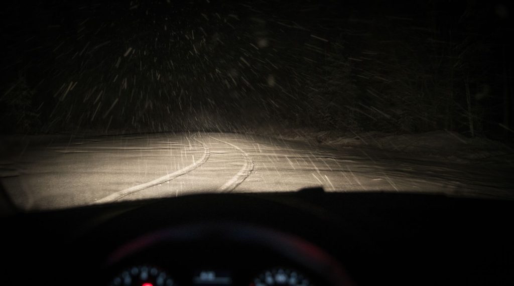 A snowy road at night seen through a car windshield.