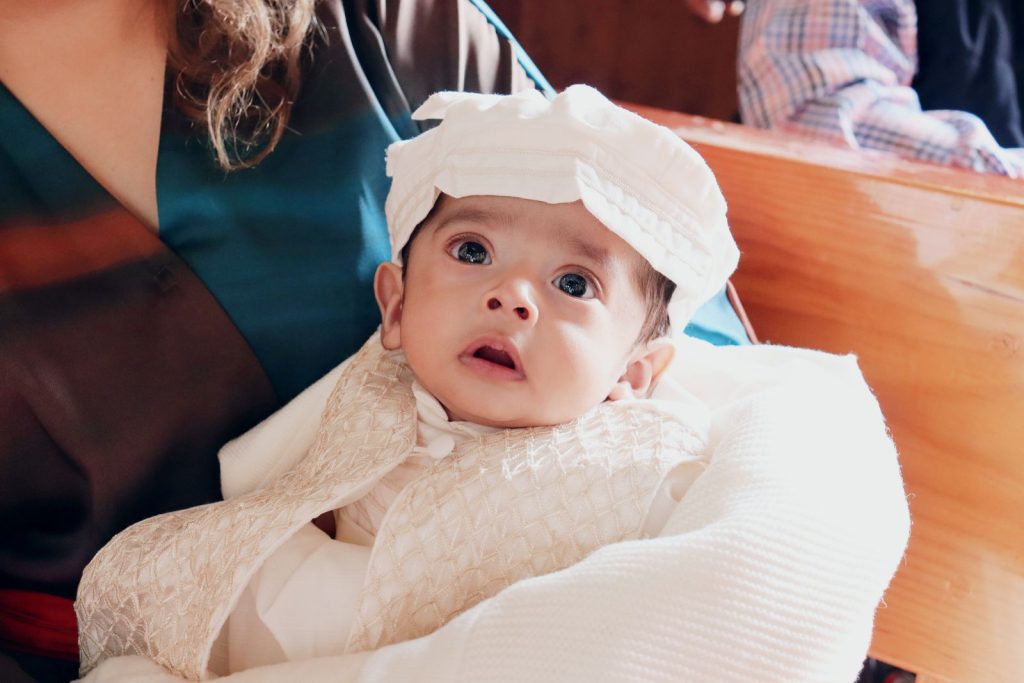 A mother holding her baby in a white christening gown in church.