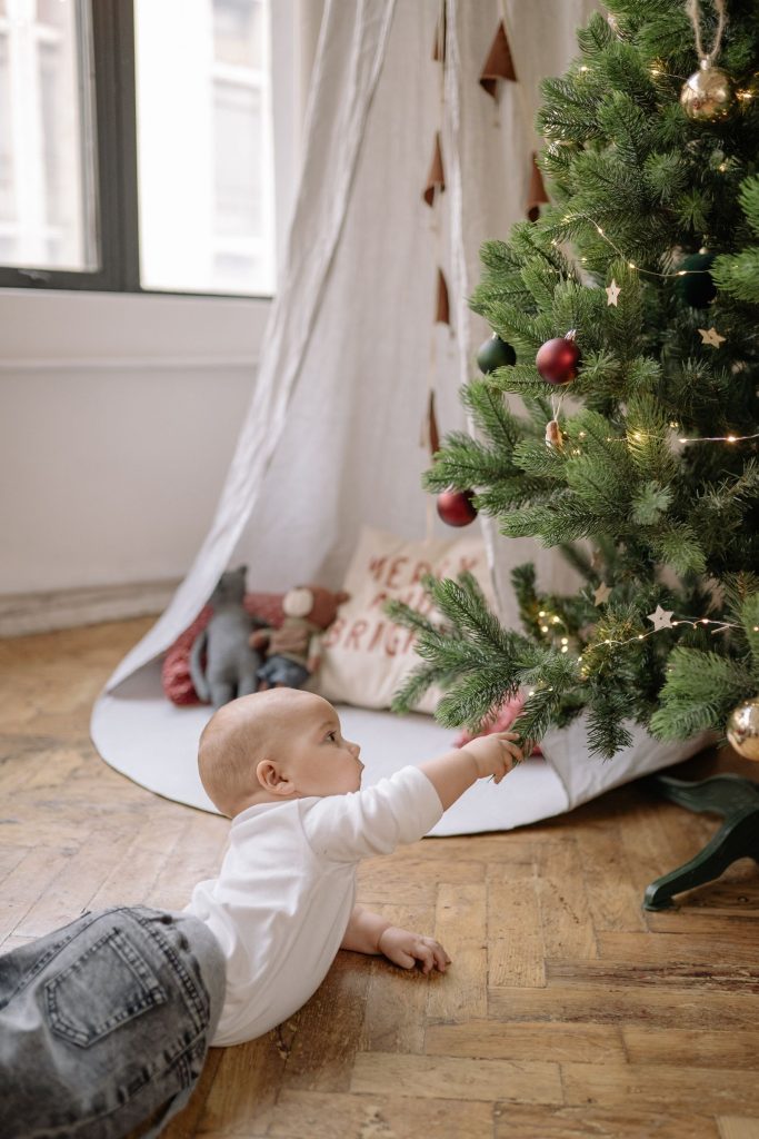 A baby reaching toward a decorated Christmas tree.