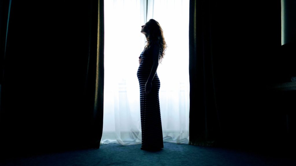 Silhouette of a pregnant woman standing by a bright window.