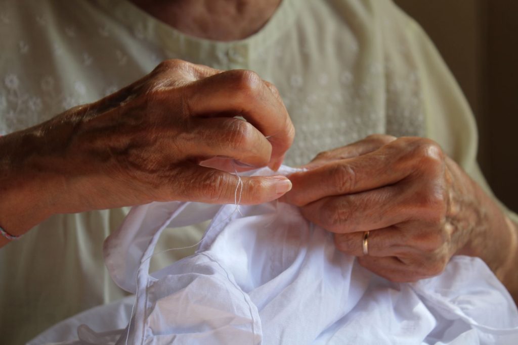 An older woman's hands sewing white fabric.
