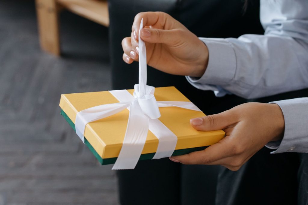 Hands untying the ribbon on a yellow gift box.