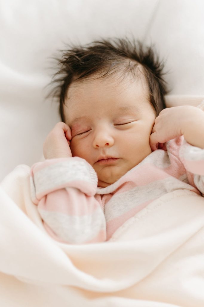 A sleeping newborn with brown hair, wrapped in a soft blanket.
