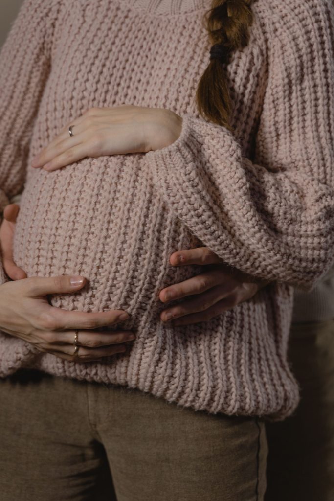 Hands resting on a pregnant woman's belly over a knit sweater.