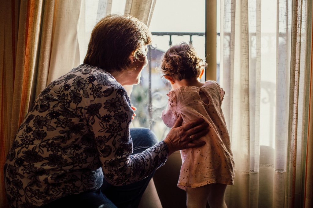 A grandmother holding a baby near a sunny window.