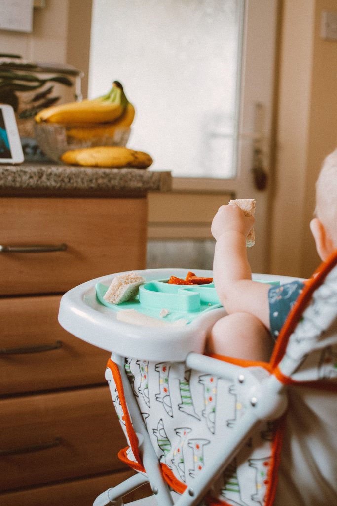 A baby in a high chair eating, seen from behind.