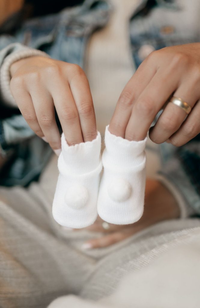 Hands holding a tiny pair of white baby socks.