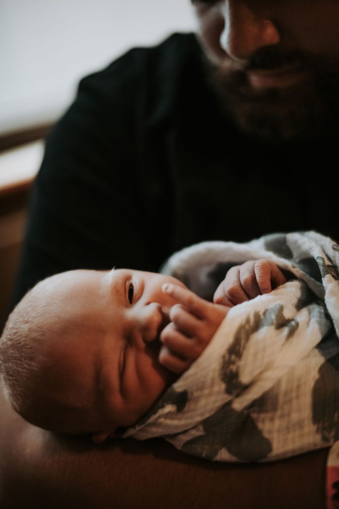 A father holding his newborn wrapped in a blanket.